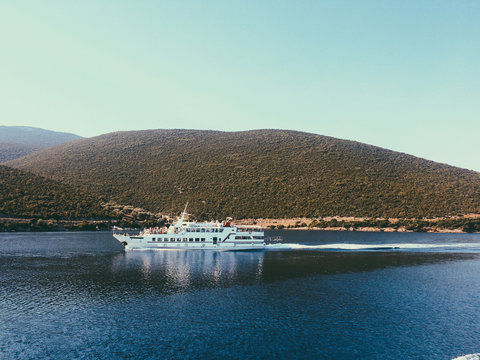 Extraordinary landscape of mountain penetrating the blue sea water. White ship with tourists floating in the Aegean sea near the mountain chain to Skyathos Island