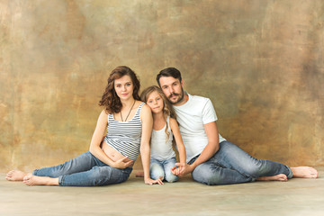 Obraz premium Pregnant mother with teen daughter and husband. Family studio portrait over brown background