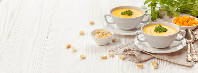 Pumpkin cream soup with croutons, raw fresh pumpkin pieces and herbs on a white rustic wooden...