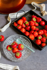 Fresh strawberries on metal, dark tray and cristal plate. Stone, gray background.
