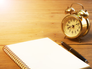 Blank notebook with vintage alarm clock and black pen on wood table