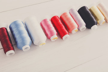 Colorful thread spools on wooden table close up