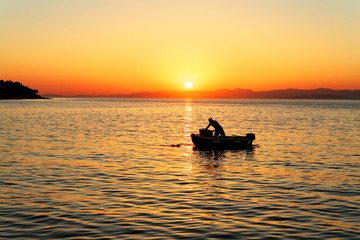 Naklejka na ściany i meble Fisherman in his boat during sunset in a harbor of small town Postira - Croatia