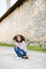 Fototapeta premium Beautiful african american girl sitting on skateboard, drinking juice.