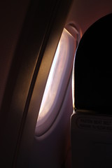Black aircraft window and backside of the passenger seat with black leather cover in the cabin crew, one airplane chair beside windowpane frame dark background and blank space template