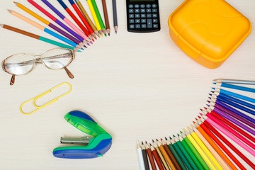 School supplies. Color pencils, yellow sandwich box, calculator, glasses, big paper clip and stapler on wooden table