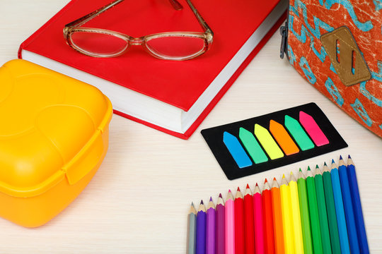 School supplies. School backpack, book, glasses, color pencils, sandwich box and color bookmarks on wooden table