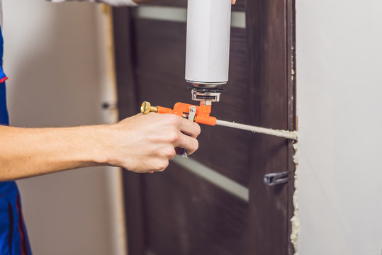 Young handyman installing door with an mounting foam in a room