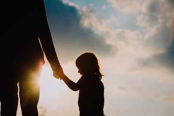 silhouette of little girl holding parent hand at sunset