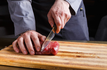 Chef cutting filet mignon on wooden board at restaurant kitchen
