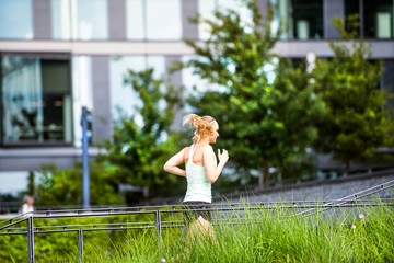 Beautiful young athlete running in front of glass buildings.