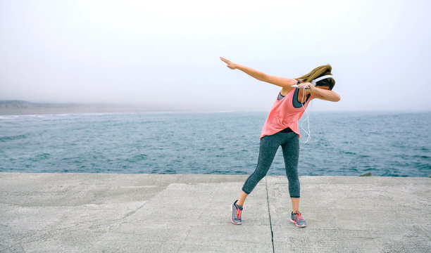 Young woman making dab dance outdoors by sea pier
