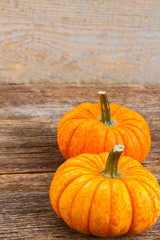 two freshly picked orange pumpkins with fall leaves on wooden textured table