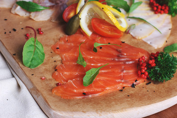Thin slices of salted trout on a wooden board with lemons and herbs