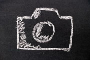 White chalk hand drawing as camera icon on black board background