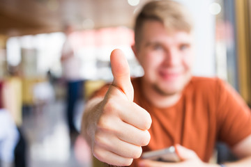technology, communication and people concept - Young man holding a smart phone with thumbs up
