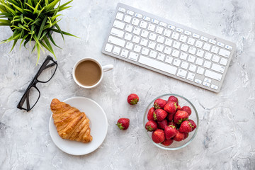 Dessert fo light lunch at workplace. Coffee, strawberry, croissant near keyboard on grey background top view