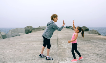 Senior sportswoman and little girl high five by sea pier