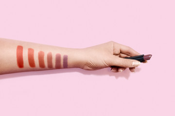 Female hand holding lipstick and color swatches painted on hand