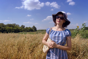 Naklejka na ściany i meble young woman standing in hat in oat field
