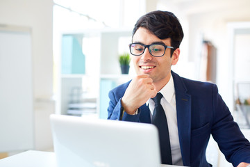 Happy specialist looking at laptop display in front of him by workplace