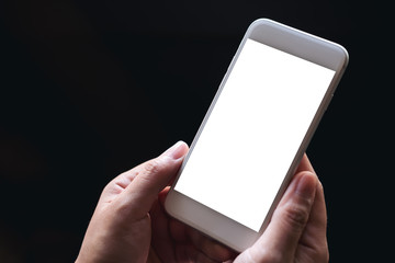 Mockup image of hands holding white mobile phone with blank screen with black background