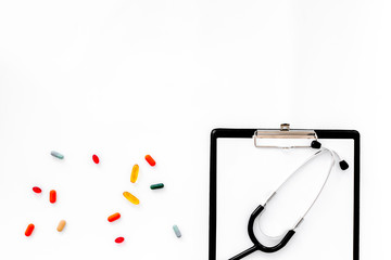 Doctor's workplace in clinic. Accessories. Clip pad, stethoscope, colored pills on white background top view copyspace