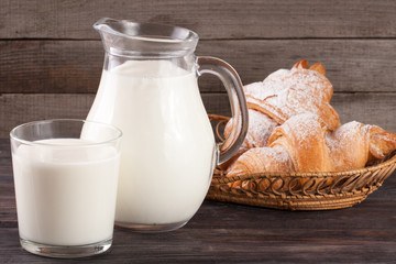 jug and glass of milk with croissants on a wooden background