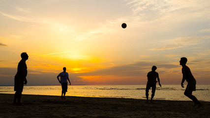 Silhouette of men playing beach volleyball at sunset.