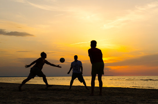 Silhouette of men playing beach volleyball at sunset.