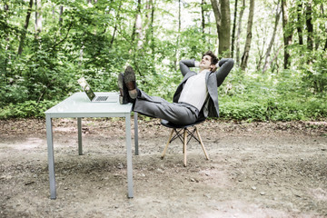 Relaxed business man in suit with heads over head and legs on office desk after successful work in green park. Freelancer relax after great deal in green forest. Business concept.