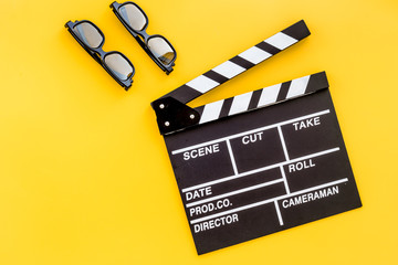 Naklejka premium Filmmaker accessories. Clapperboard and glasses on yellow background top view copyspace