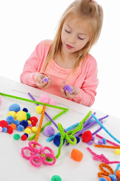 fillette 6 ans jouant avec des pompons de couleurs et des fils chenille