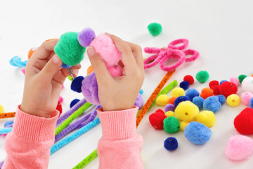 fillette 6 ans jouant avec des pompons de couleurs et des fils chenille © mariesacha