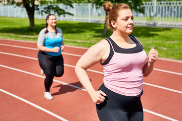 Active and determined over-sized women jogging on stadium in the morning