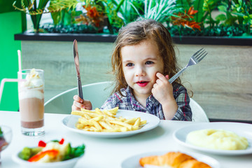 Little girl having lunch in the restaurant with the table knife and fork in hands.