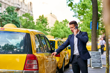 Young businessman walking to a taxi and talking on a phone