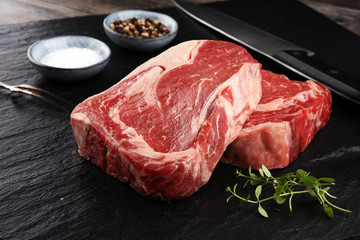 Raw fresh meat Ribeye Steak, seasoning and meat fork on dark background