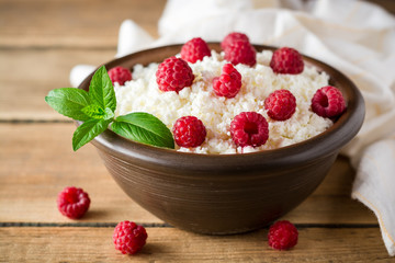 Cottage cheese with raspberry and mint in ceramic bowl on rustic wooden table