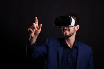 Businessman in suit with a VR headset on head touching a virtual button in studio photo on black background. Virtual reality and gestures