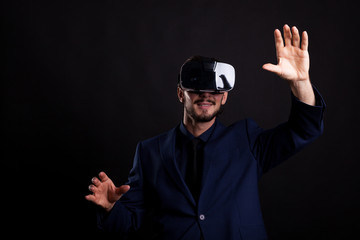 Businessman with a VR headset on head in studio photo on black background. Virtual reality and gestures