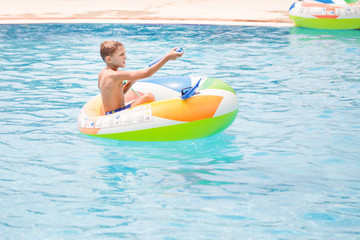 Little boy sitting in inflatable boat and having fun with water gun