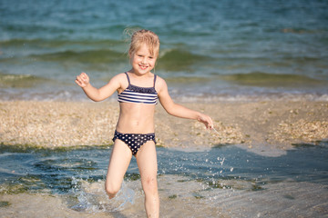 Little cute blonde girl running along the beach
