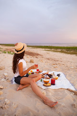 Woman in summer Picnic on the beach at sunset in the white plaid, food and drink conception