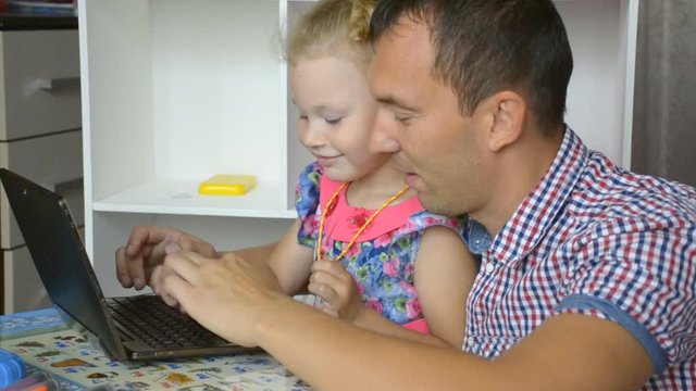A little girl and her father are playing at home in the tablet.