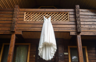 Beautiful long wedding dress hanging on the balcony of wooden house outdoors, free space