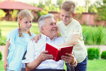 Happy old grandfather reading book for cute children  in garden