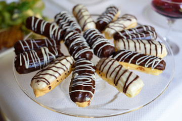 Beautiful homemade eclairs filled with vanilla and chocolate custard on plate, selective focus. Traditional French dessert. Fresh baked eclair with chocolate glaze on top