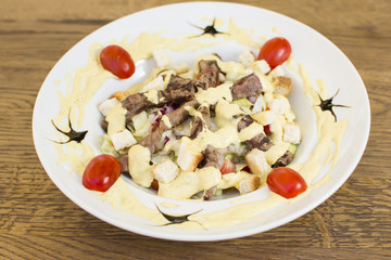 Healthy grilled red meat salad with cheese and croutons. Bacon and lettuce slices in a white plate on a wooden table.