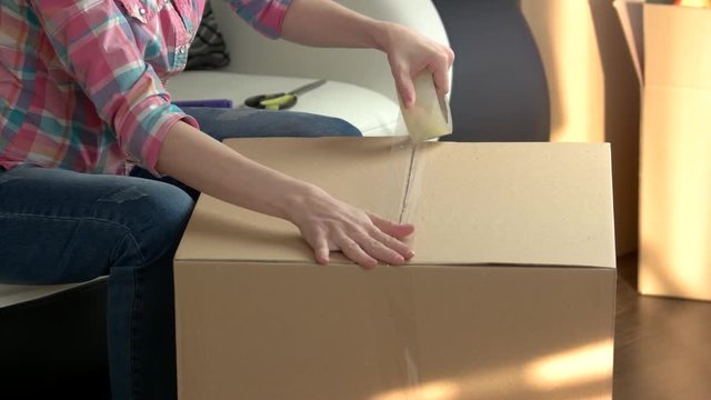 Woman packing box. Cardboard box with adhesive tape. Average moving cost.